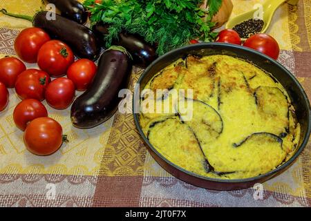 Hot ready moussaka in the form for baking among vegetables and spicy herbs. Fresh vegetables for cooking light dinner, Moussaka - a traditional Greek Stock Photo