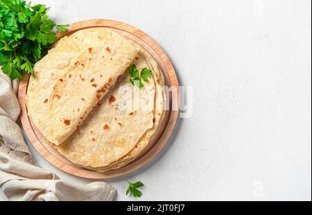 Traditional Indian chapati cakes on a wooden board with fresh herbs on a gray background. Stock Photo