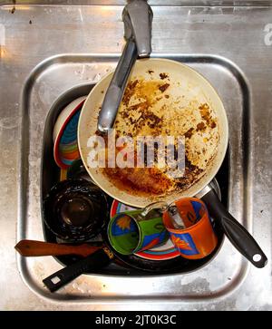 mass of dirty dishes with food scraps waiting to be washed in the metal sink after a festive dinner Stock Photo