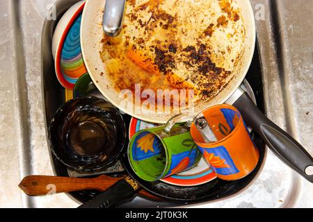 mass of dirty dishes with food scraps waiting to be washed in the metal sink after a festive dinner Stock Photo
