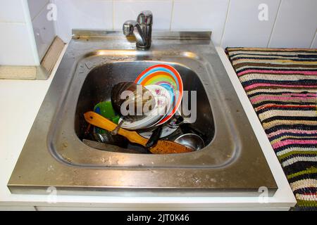 mass of dirty dishes with food scraps waiting to be washed in the metal sink after a festive dinner Stock Photo