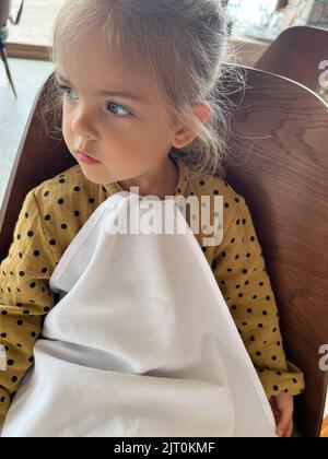 Little girl with a napkin tucked into her collar sits in a restaurant Stock Photo