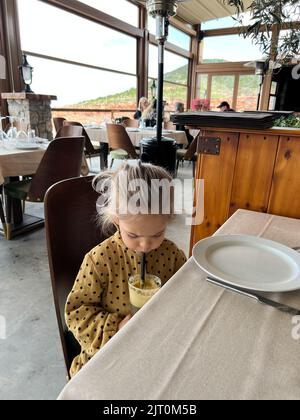Little girl drinking a drink from a straw at a table in a restaurant Stock Photo