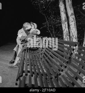 In the 1950s. A young couple is sitting on a bench kissing. A date ending pretty well. Sweden 1953 Conard ref 2402 Stock Photo