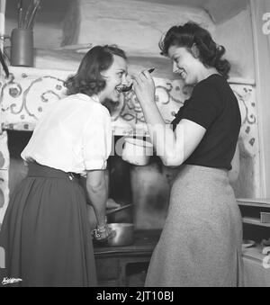 In the kitchen 1940s. Interior of a rural kitchen and two women cooking together, one tasting from the content of a stew on a spoon. Sweden 1945 Kristoffersson ref N143-5 Stock Photo