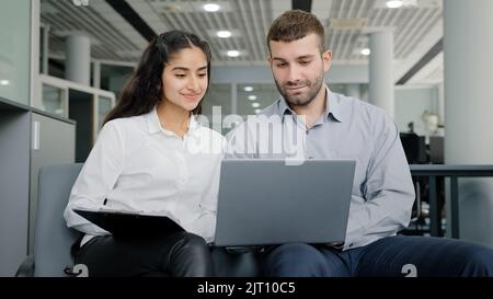 Young man and woman office workers creative team colleagues discussing online project develop strategy using laptop exchange ideas talks in workplace Stock Photo