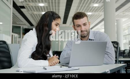 Young recruit woman presenting project on laptop to mentor professional female manager training new male worker explains online services to client on Stock Photo