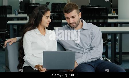 Friendly colleagues communicate sitting in office promising young woman manager showing presentation on laptop explaining project details to mentor Stock Photo
