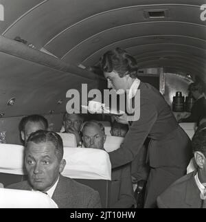 Airline travelling in the 1960s. A group of women and  men on an swedish passenger airplane in the 1960s. The female flight attendant is standing in the middle of the airplane serving coffee and sandwiches to the passengers. Sweden 1960 Kristoffersson ref CG39-11 Stock Photo