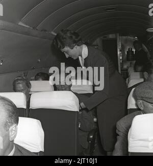 Airline travelling in the 1960s. A group of women and  men on an swedish passenger airplane in the 1960s. The female flight attendant is standing in the middle of the airplane servicing with something. Sweden 1960 Kristoffersson ref CG39-12. Stock Photo