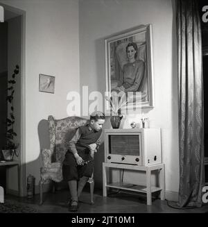 In the 1940s. A young boy at home is listening to the radio. He is sitting in an armchair and focuses on the sound from the radioset that is standing beside him. A radio manufactured by Telefunken. He is wearing the typical 1940s golf trousers and holds his favorite toy in his hand, a metal airplane. Sweden 1946 Kristoffersson ref Y118-6 Stock Photo