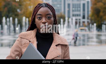 Close-up pensive serious african american woman standing in autumn city young girl student manager freelancer focused looking at camera confident Stock Photo