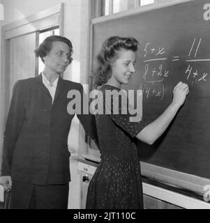 School in the 1940s. A teacher in front of the classroom at the black board with one of the students who is solving a mathematic calculation. The teacher is Mrs Aina Erlander, wife of the swedish prime minister Tage Erlander.  Sweden 1946 Stock Photo