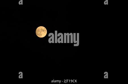 Full moon glows orange against deep black night sky Stock Photo