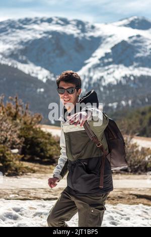 Handsome caucasian man posing to camera. He carries his cell phone and sunglasses. he has snowy mountains in the background Stock Photo