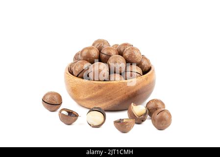Inshell macadamia nuts in a wooden bowl and several nuts are peeled on a white background. Copy space. Stock Photo