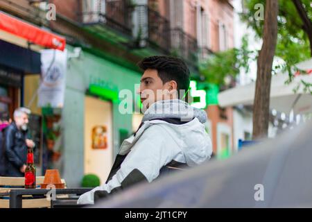 handsome masculine man with a coat sitting at a restaurant table outside Stock Photo