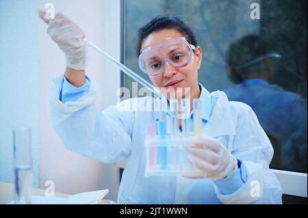 Confident pharmacologist, medical biologist, laboratory assistant using glass pipette, pipetting liquid into test tubes Stock Photo