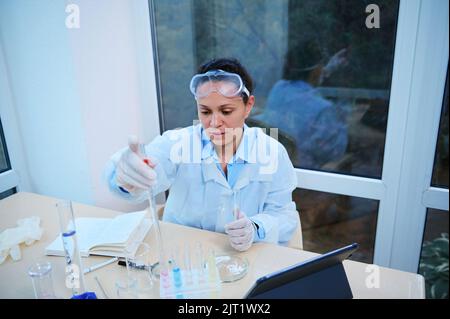 Hispanic woman pharmacologist makes an analysis of substances. Pharmacist scientist works in pharmacological laboratory Stock Photo