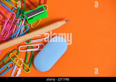 Stationery for schoolchildren paper clips, pencil, eraser and sharpener on an orange background Stock Photo
