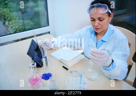 Multi-ethnic woman, pharmacologist in white lab coat, working on development of new medical drug in research laboratory Stock Photo