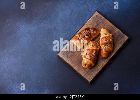 Delicious homemade pastries with apricot jam sprinkled with sesame seeds on a wooden cutting board against a blue concrete background Stock Photo