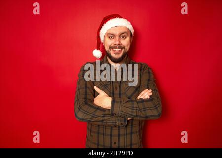 smiling man in new year hat, casual clothes with arms folded in front isolated red studio background Stock Photo