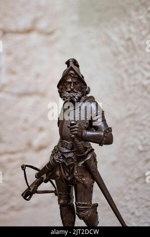 A vertical closeup shot of an ancient bronze statuette of a warrior soldier with armor, sword, and a crossbow Stock Photo