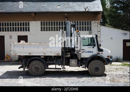 A side view of a white Mercedes Benz Unimog G5000 off-road truck with a crane in front of a building Stock Photo
