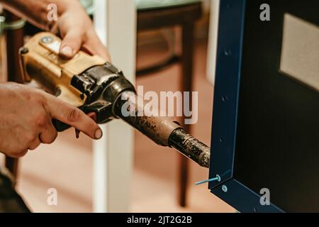 Male worker uses electric riveting gun. Hand holding  riveting machine and placing rivets. Working workshop of carpenter or mechanic. Stock Photo