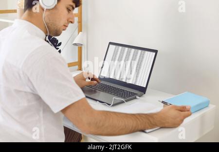 Man sitting at desk with laptop, working with business spreadsheets, and taking notes in notebook Stock Photo