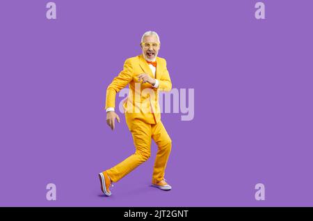 Cheerful trendy, eccentric and energetic senior man funny dancing isolated on purple background. Stock Photo