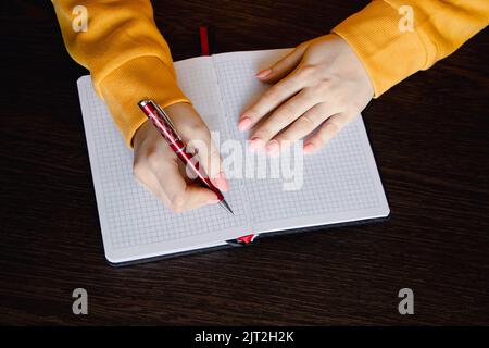 Woman writing in blank notebook. Close-up of hand holding pen. Businesswoman takes notes in office. Stock Photo