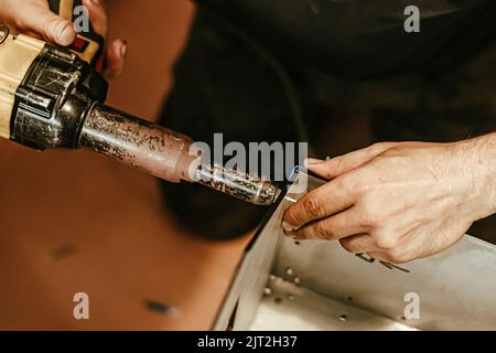 Male worker uses electric riveting gun. Hand holding riveting machine and placing rivets. Working workshop of carpenter or mechanic. Stock Photo