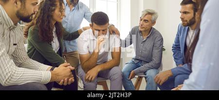 People supporting and comforting a depressed young man during a group therapy session Stock Photo