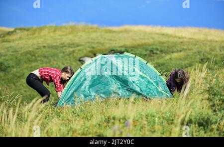 Girls set up tent on top mountain. Camping trip. Helpful to have partner for raising tent. Camping skills concept. Camping and hiking. In middle of Stock Photo