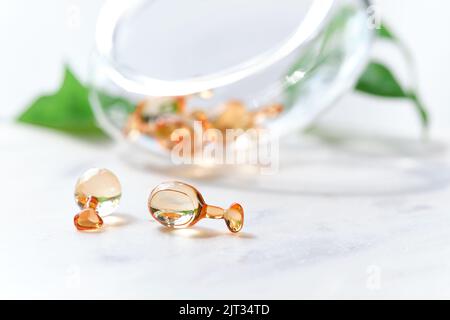 Serum capsules for healthy skin. Blurred background, glass jar with the capsules and green palm leaf. Stock Photo