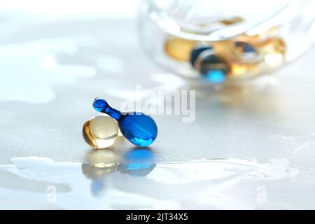 Various serum capsules for healthy skin routine. Blurred background, glass jar with the capsules on wet table. Stock Photo