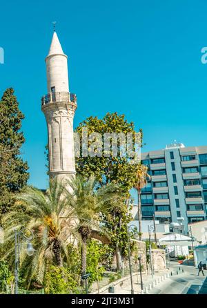 A vertical shot of Djami Kebir Mosque between the trees and palms in Larnaca, Cyprus Stock Photo