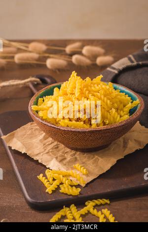 fusilli pasta in wooden cutting board on rustic kitchen countertop. Stock Photo