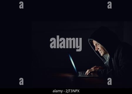 You wont even see him coming. a hooded computer hacker using a laptop in the dark. Stock Photo