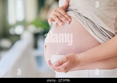 Preventing pregnancy stretch marks. a woman applying cream to her pregnant belly. Stock Photo