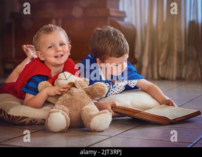 Sparking their imaginations at story time. Portrait of a happy little boy listening to his brother read a story while they lie on the floor at home. Stock Photo