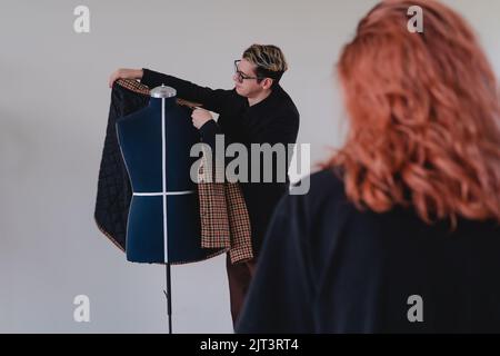 Tailor showing a suit to a female client. Tailor selling a suit. Fashion designer arranging a suit on a mannequin. High quality photo Stock Photo