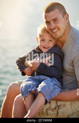 Every father is his sons first hero. Portrait of a father bonding with his little boy while they sit by the harbor. Stock Photo