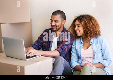 Our new home has great wifi. a young couple using a laptop while sitting among boxes on moving day. Stock Photo