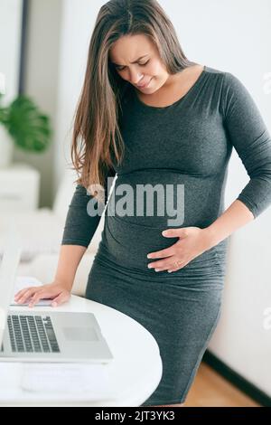 That was quite the kick. a young pregnant woman feeling unwell while working from home. Stock Photo