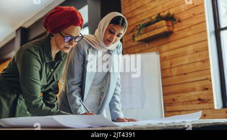 Two Muslim architects working together on a creative project in an office. Innovative businesswomen working on blueprint drawings. Two female architec Stock Photo