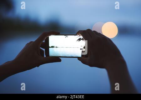 Great pictures, even in low light conditions. an unidentifiable young woman photographing a dusky landscape with her phone. Stock Photo