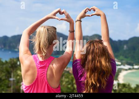 Keep on loving life. Rear view shot of two young woman making a heart gesture while facing a scenic landscape. Stock Photo